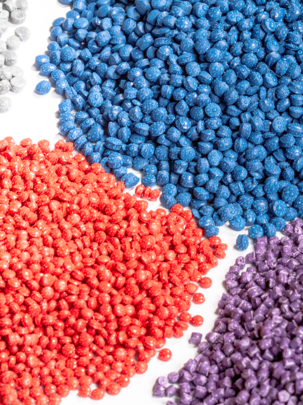 Close-up of multi-colored granules against a white background, showcasing raw materials used in the plastic and polymers industry with PerMix solutions